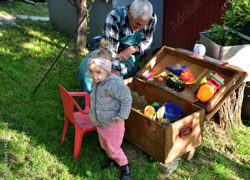Grandfather plays with his granddaughter in the sandbox with sand moulds