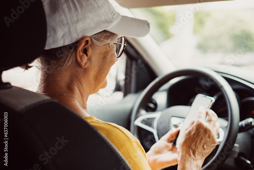 Senior woman stops driving the car to use smartphone, elderly female satisfied with unforgettable journey by car, sits on driver`s seat. People, driving, transport concept