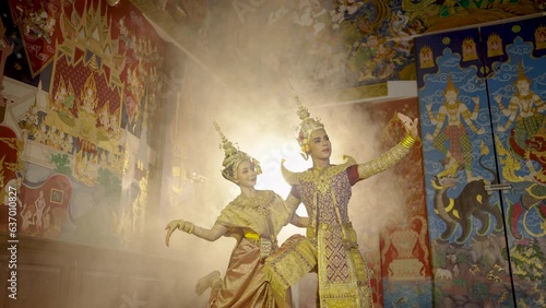 Beautiful Asian woman wear Thai traditional dress action of dancing together with man stand in front of Thai painting on public place wall.