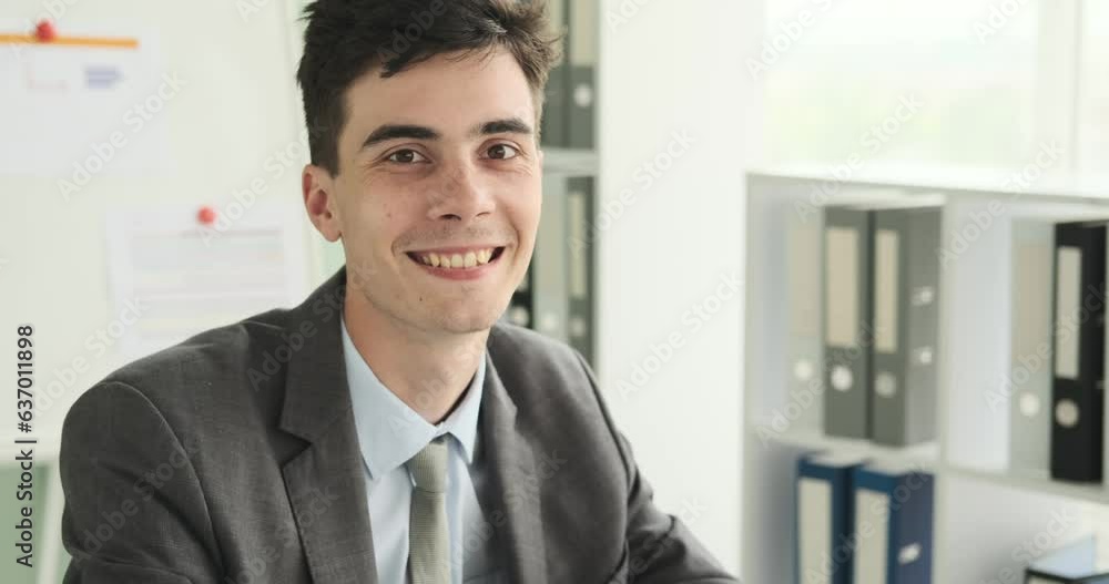 Smiling businessman is seen looking directly into the camera. With a friendly and approachable smile, he exudes confidence and positivity. The office setting reflects a professional environment. Smiling businessman is seen looking directly into the camera. With a friendly and approachable smile, he exudes confidence and positivity. The office setting reflects a professional environment.