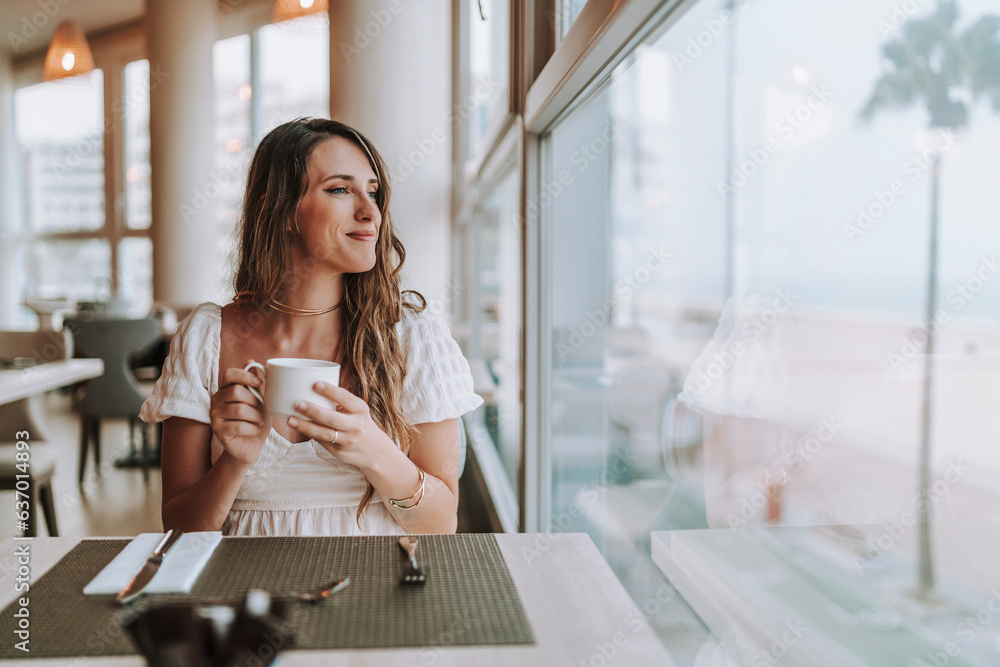 Chica joven tomando café en cafetería de hotel mientras mira por la ventana