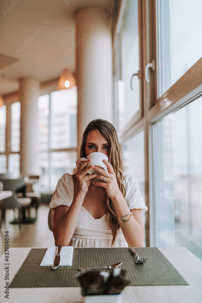 Chica joven tomando café en cafetería de hotel mientras mira por la ventana