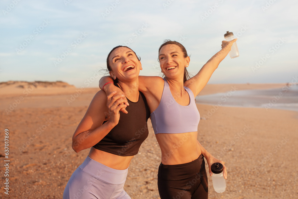 Satisfied cheerful young caucasian women hugs, enjoy morning workout, have fun with water bottles Satisfied cheerful young caucasian women hugs, enjoy morning workout, have fun with water bottles