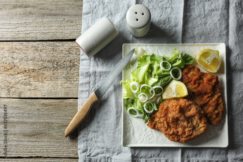 Tasty schnitzels served with lemon and salad on wooden table, flat lay. Space for text Tasty schnitzels served with lemon and salad on wooden table, flat lay. Space for text