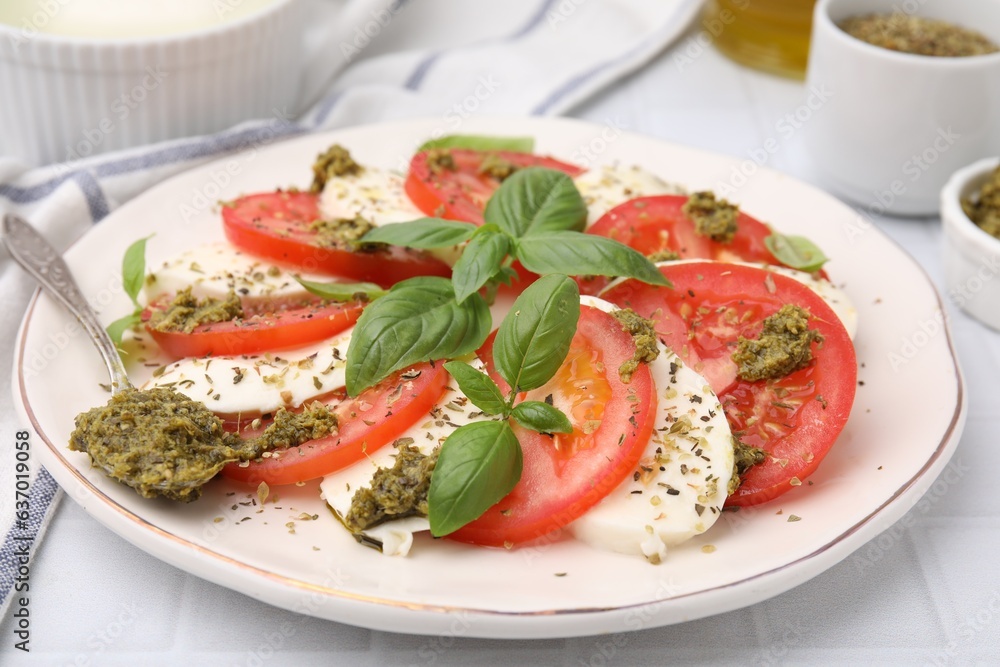 Plate of delicious Caprese salad with pesto sauce on white tiled table, closeup Plate of delicious Caprese salad with pesto sauce on white tiled table, closeup