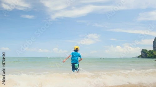 Child alone on the sea beach plays in the water during a sunny day in a sial in Pacific Asia with the waves of the sea free happy active and childhood vacations photo