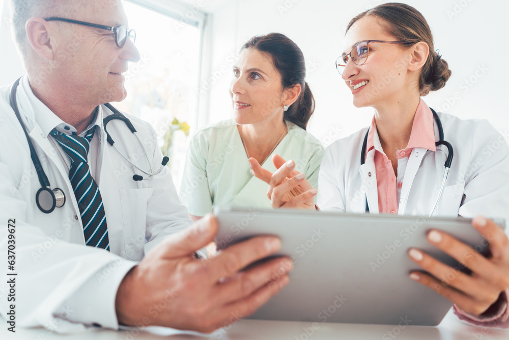 Team of doctors in meeting discussing a case looking at technology Team of doctors in meeting discussing a case looking at technology