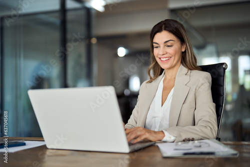 Happy mature business woman entrepreneur in office using laptop at work, smiling professional middle aged 40 years old female company executive wearing suit working on computer at workplace. © insta_photos