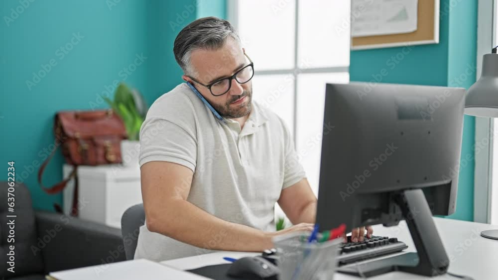 Grey-haired man business worker using computer talking on smartphone at the office Grey-haired man business worker using computer talking on smartphone at the office