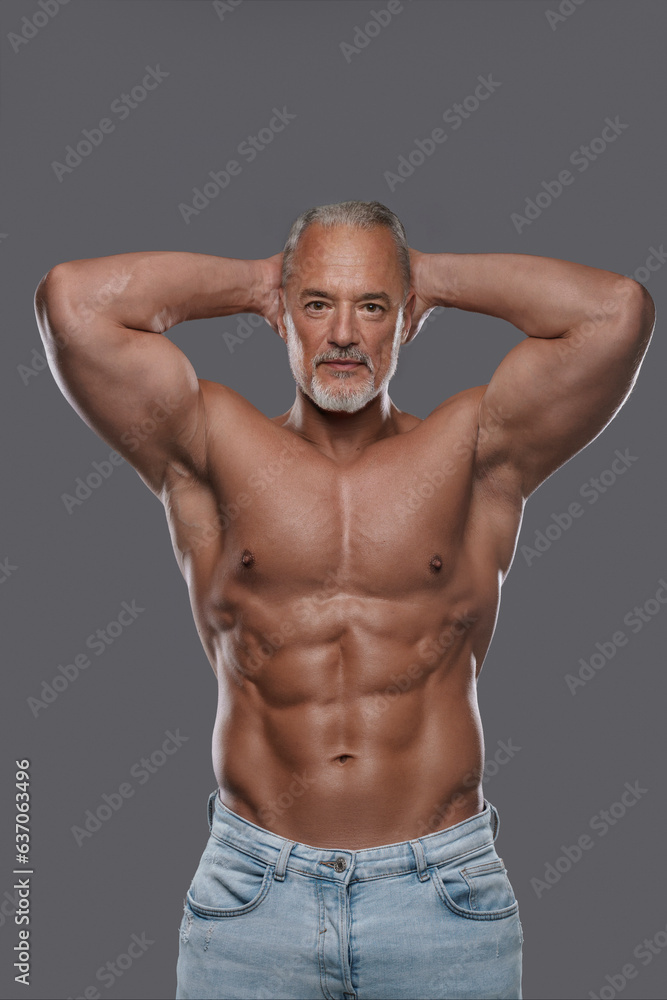 This attractive mature muscular man with a stylish salt and pepper beard poses shirtless in ripped jeans against a grey backdrop This attractive mature muscular man with a stylish salt and pepper beard poses shirtless in ripped jeans against a grey backdrop
