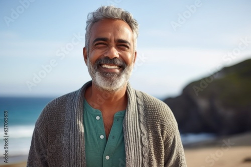 Medium shot portrait of an Indian man in his 50s against a beach background wearing a chic cardigan