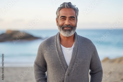 Medium shot portrait of an Indian man in his 50s against a beach background wearing a chic cardigan