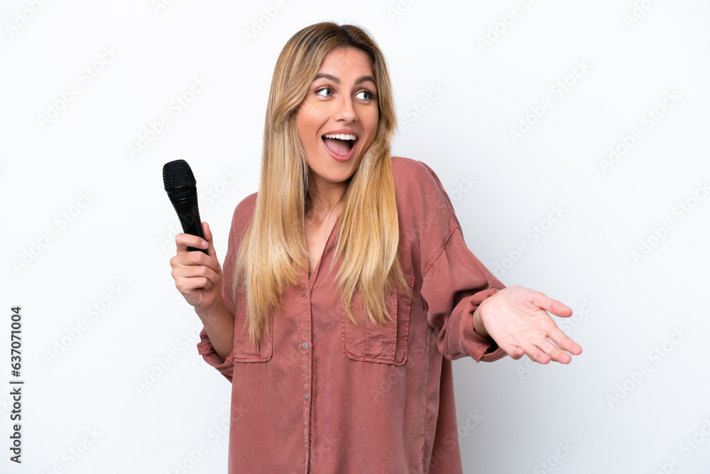 Singer Uruguayan woman picking up a microphone isolated on white background with surprise expression while looking side Singer Uruguayan woman picking up a microphone isolated on white background with surprise expression while looking side