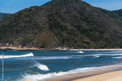 Grumari beach near Barra da Tijuca in Rio de Janeiro, Brazil. Sunny day with blue sky, clear water and small waves. Hills and nature around