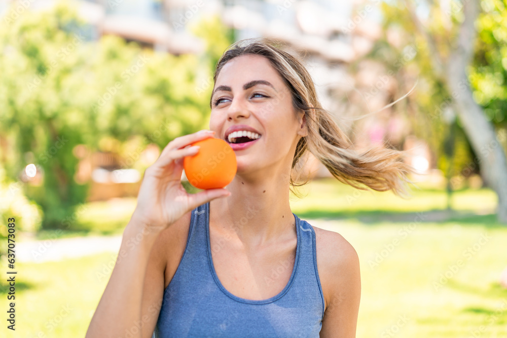 Young blonde woman at outdoors holding an orange with happy expression Young blonde woman at outdoors holding an orange with happy expression