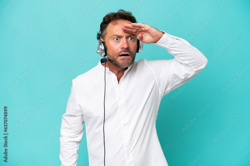 Telemarketer caucasian man working with a headset isolated on blue background looking far away with hand to look something