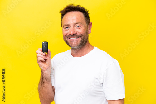 Middle age caucasian man holding car keys isolated on yellow background smiling a lot