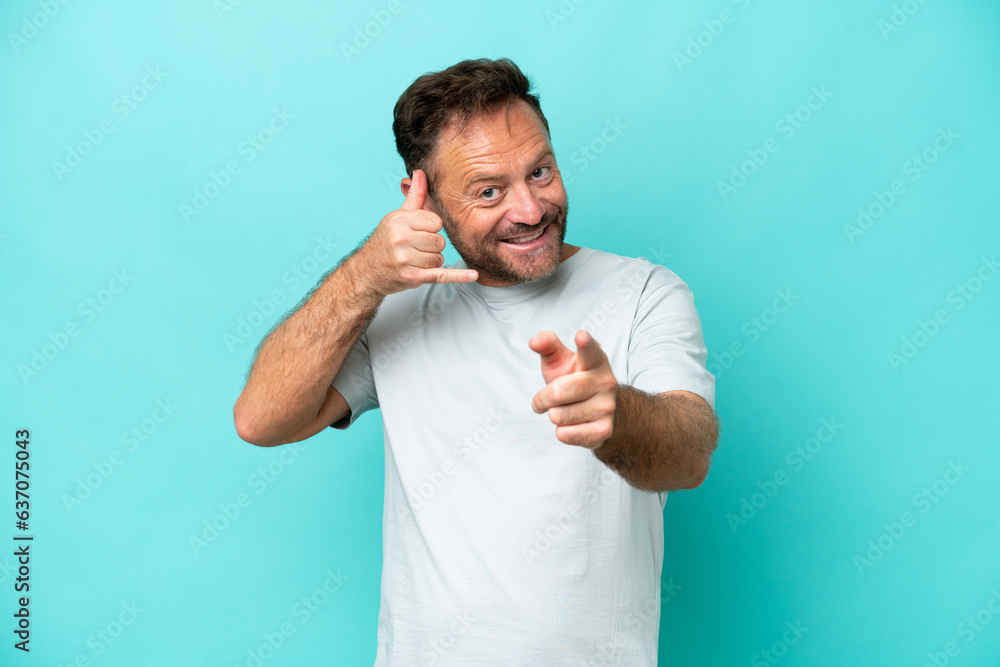 Middle age caucasian man isolated on blue background making phone gesture and pointing front Middle age caucasian man isolated on blue background making phone gesture and pointing front