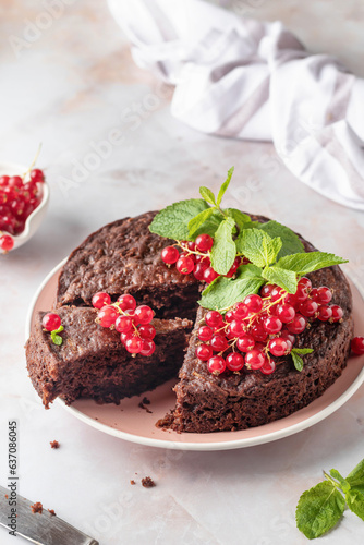 Cutted Tasty homemade chocolate cake brownie decorated with red currant berries and mint on white marble table