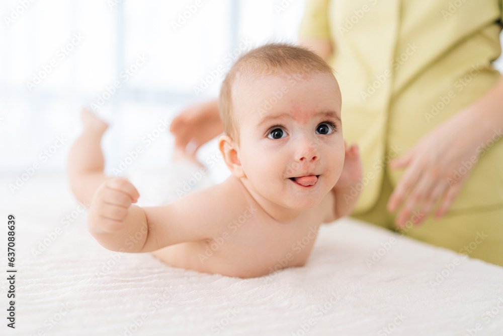 Closeup portrait of adorable infant baby boy lying on white blanket on stomach, smiling looking away, during back massage. Concept of children, baby, parenthood, childhood, life, maternity, motherhood Closeup portrait of adorable infant baby boy lying on white blanket on stomach, smiling looking away, during back massage. Concept of children, baby, parenthood, childhood, life, maternity, motherhood