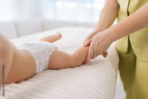 Closeup cropped shot of unrecognizable loving mom helping doing gymnastics exercise massaging to newborn son. Close up hands of professional female masseuse doing exercises with infant baby legs, feet