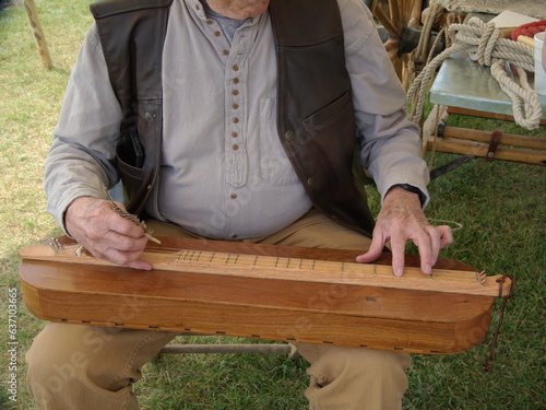 The builder of this dulcimer plays a tune, using a feather to pluck the strings while he chooses the notes on the fret with his other hand. photo