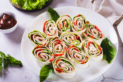 Foto Rolled up sandwiches with lettuce, bacon and baked peppers in a tortilla on a pl