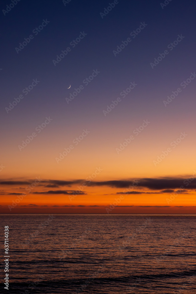 Fototapeta premium The moon above ocean during sunset