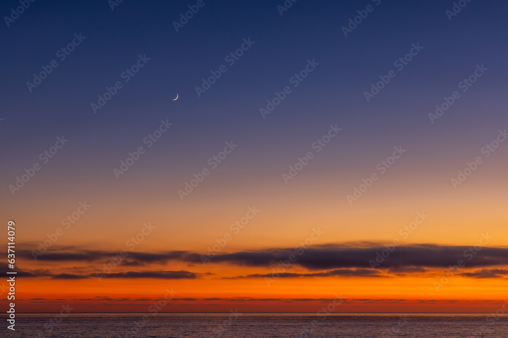 The moon above ocean during sunset