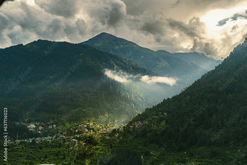 Obraz premium a cloudy sky over mountains with cows grazing on the side