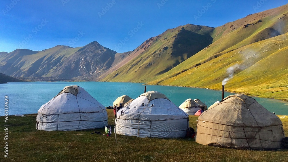 Scenic landscape featuring yurts near a lake with majestic mountains in the background. Kyrgyzstan.