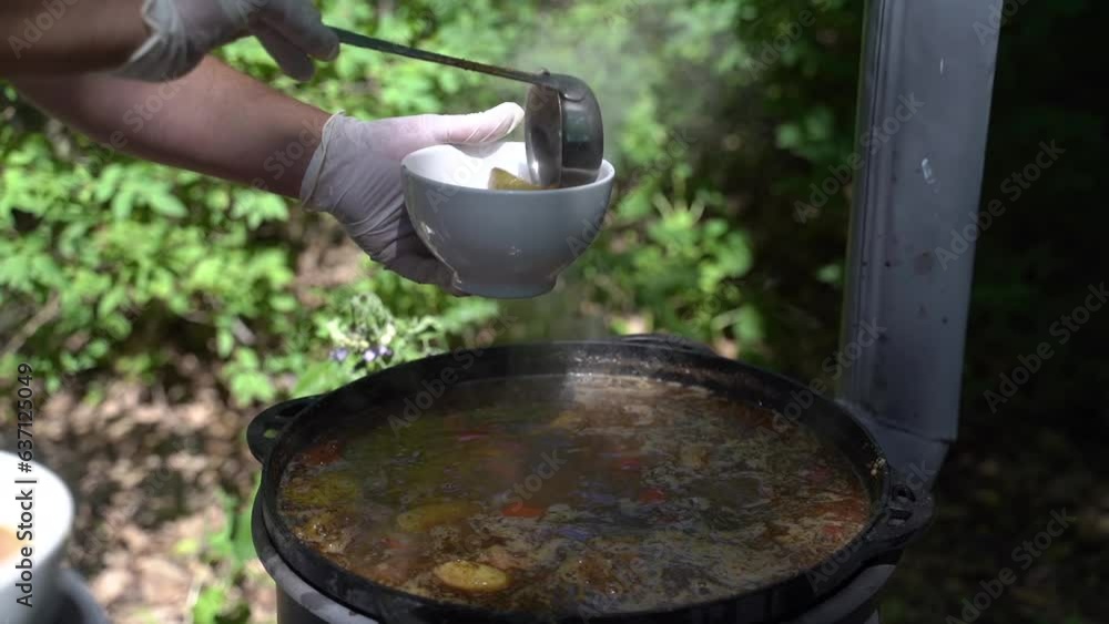 The cook pours meat soup in a cast-iron cauldron on plates. Slow motion The cook pours meat soup in a cast-iron cauldron on plates. Slow motion