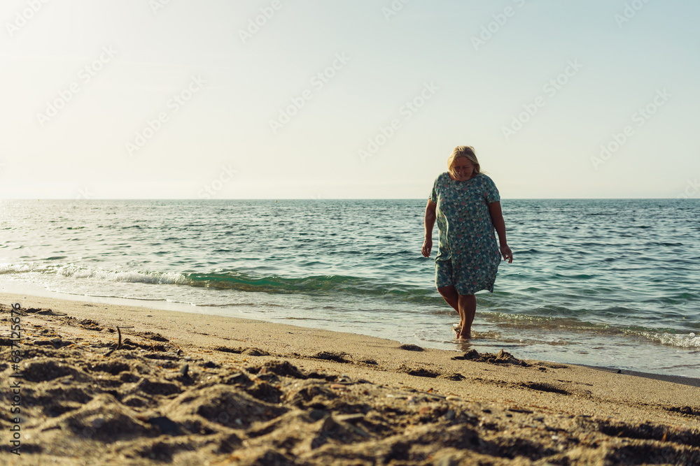 beautiful grandmother blonde in a dress walks on the sand on the beach near the sea vacation pension travel