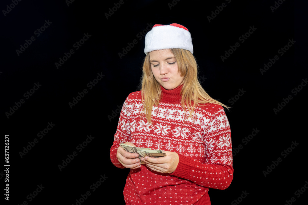 young blonde blue-eyed girl poses on black background with money. A woman with light hair and eyes in a sweater and a Christmas hat shows an astonished face when counting money. young blonde blue-eyed girl poses on black background with money. A woman with light hair and eyes in a sweater and a Christmas hat shows an astonished face when counting money.