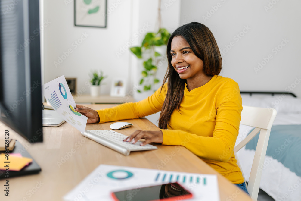 Latin young college student with holding documents while using desktop computer. Millennial young woman sitting at desk studying online at home. Latin young college student with holding documents while using desktop computer. Millennial young woman sitting at desk studying online at home.