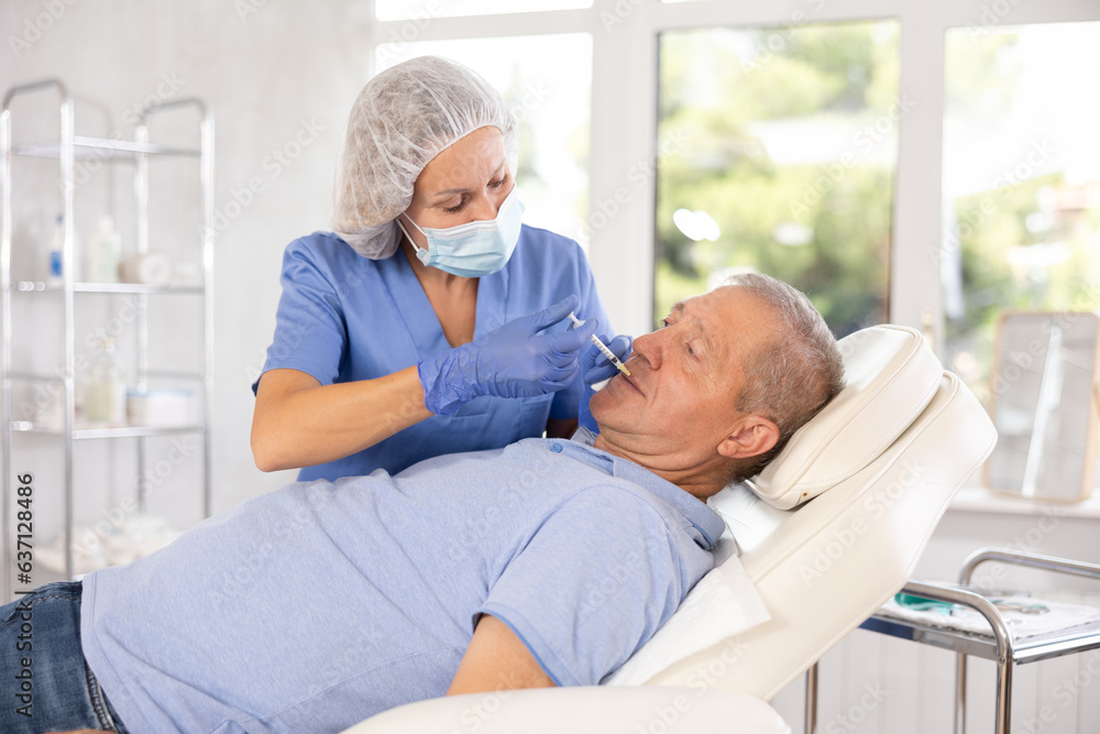 Obraz premium Old man having face mesotherapy implemented by middle-aged dermatologist in aesthetic clinic