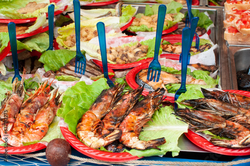 Street food at the market in Catania, Sicily island, Italy. Grilled shrimp served on a red plate with a blue fork,seafood at the market