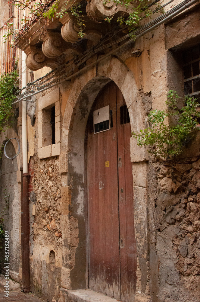 Old wooden door in a stone wall.Narrow street of the old city.Syracuse,Italy.