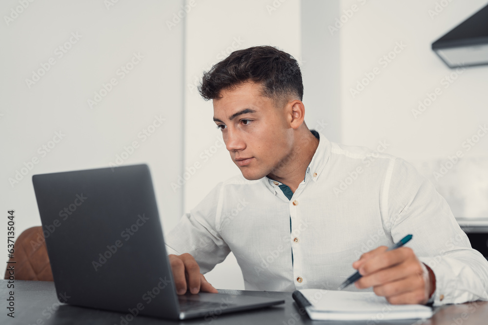 Side view handsome young businessman in eyewear working with computer remotely, sitting at wooden table in office. Pleasant happy man communicating in social network, searching information online.. Side view handsome young businessman in eyewear working with computer remotely, sitting at wooden table in office. Pleasant happy man communicating in social network, searching information online..