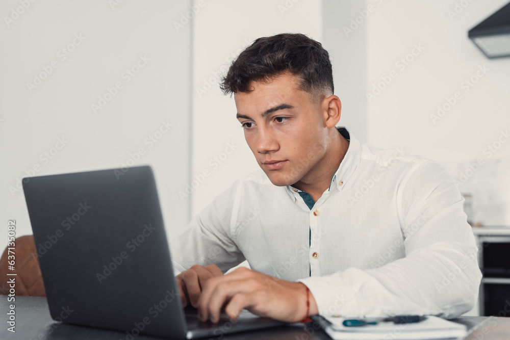 Side view handsome young businessman in eyewear working with computer remotely, sitting at wooden table in office. Pleasant happy man communicating in social network, searching information online.. Side view handsome young businessman in eyewear working with computer remotely, sitting at wooden table in office. Pleasant happy man communicating in social network, searching information online..