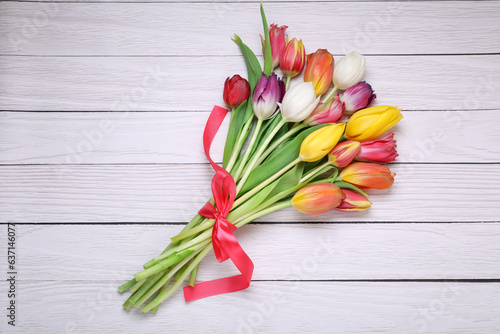 Bouquet of beautiful colorful tulip flowers tied with red ribbon on white wooden table, top view