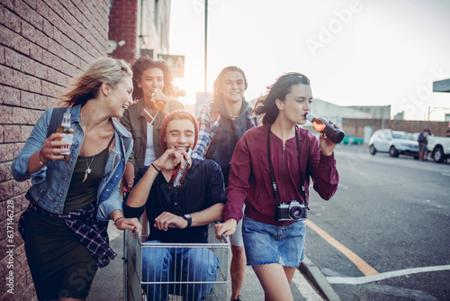 Diverse group of young people having a beer and having fun with a shopping cart on a city sidewalk photo