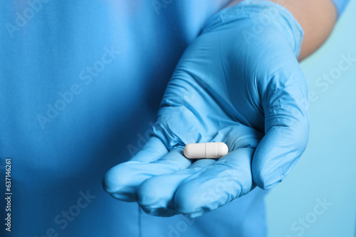 Doctor in medical glove holding pill on turquoise background, closeup