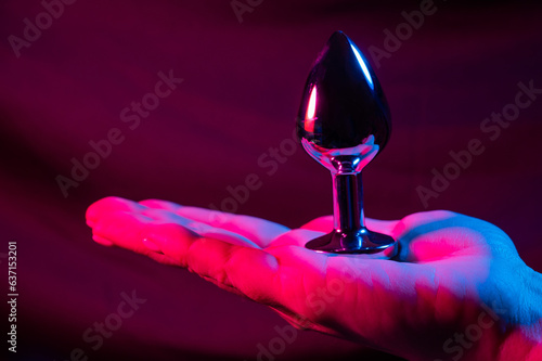 Woman holding metal anal plug in neon pink purple light. 