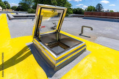 Roof hatch for access to roof with a built in skylight on a spray foam roof with painted yellow walking path

