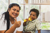Happy cheerful asian mother sitting thumbs up raising on sofa playing with cute and naive son in living room : Thai mother raises a lovely 10-month old son of Thai African American Nigerian descent.