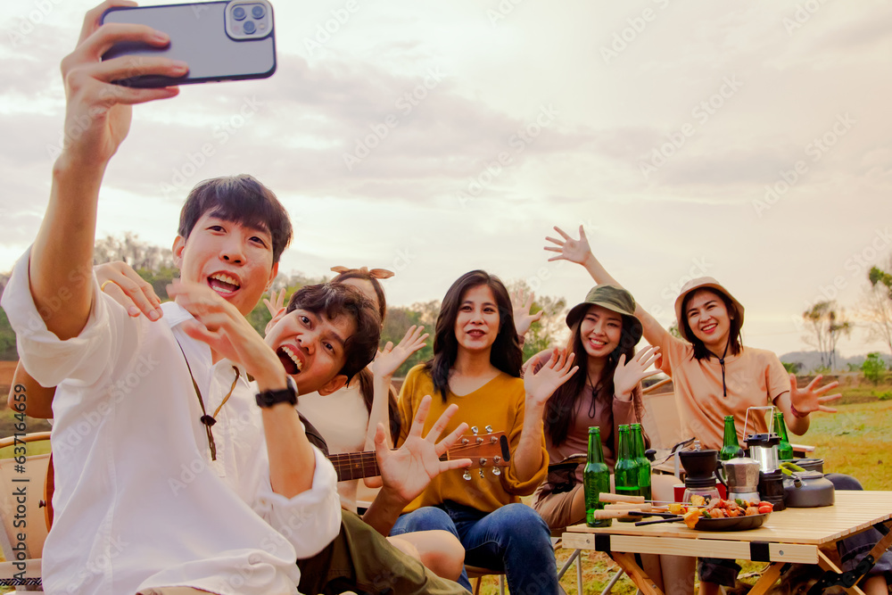 Obraz premium Group of best friends men and women hilarious party together taking selfies on the table camping taking pictures with smartphones having fun on vacation in the forest and mountains evening sunset.