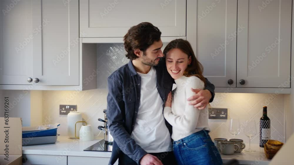 Loving couple hugging in kitchen of new home as they unpack boxes on moving in day together - shot in slow motion Loving couple hugging in kitchen of new home as they unpack boxes on moving in day together - shot in slow motion
