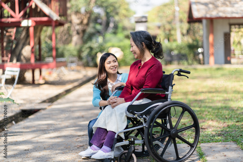 Obraz premium Asian senior woman in wheelchair with happy daughter. Family relationship retired woman sitting on wheelchair in the park age care at retirement home.