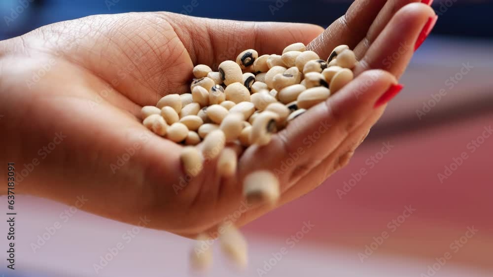 The text describes a hand holding black and white beans, a close up of a woman's hand, and a red table The text describes a hand holding black and white beans, a close up of a woman's hand, and a red table
